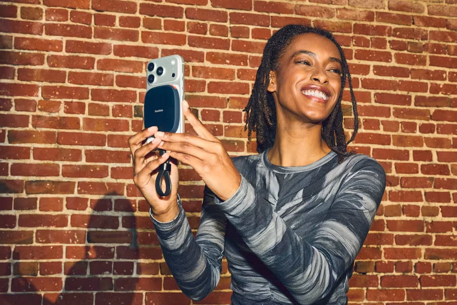A smiling woman taking a photo against a brick wall