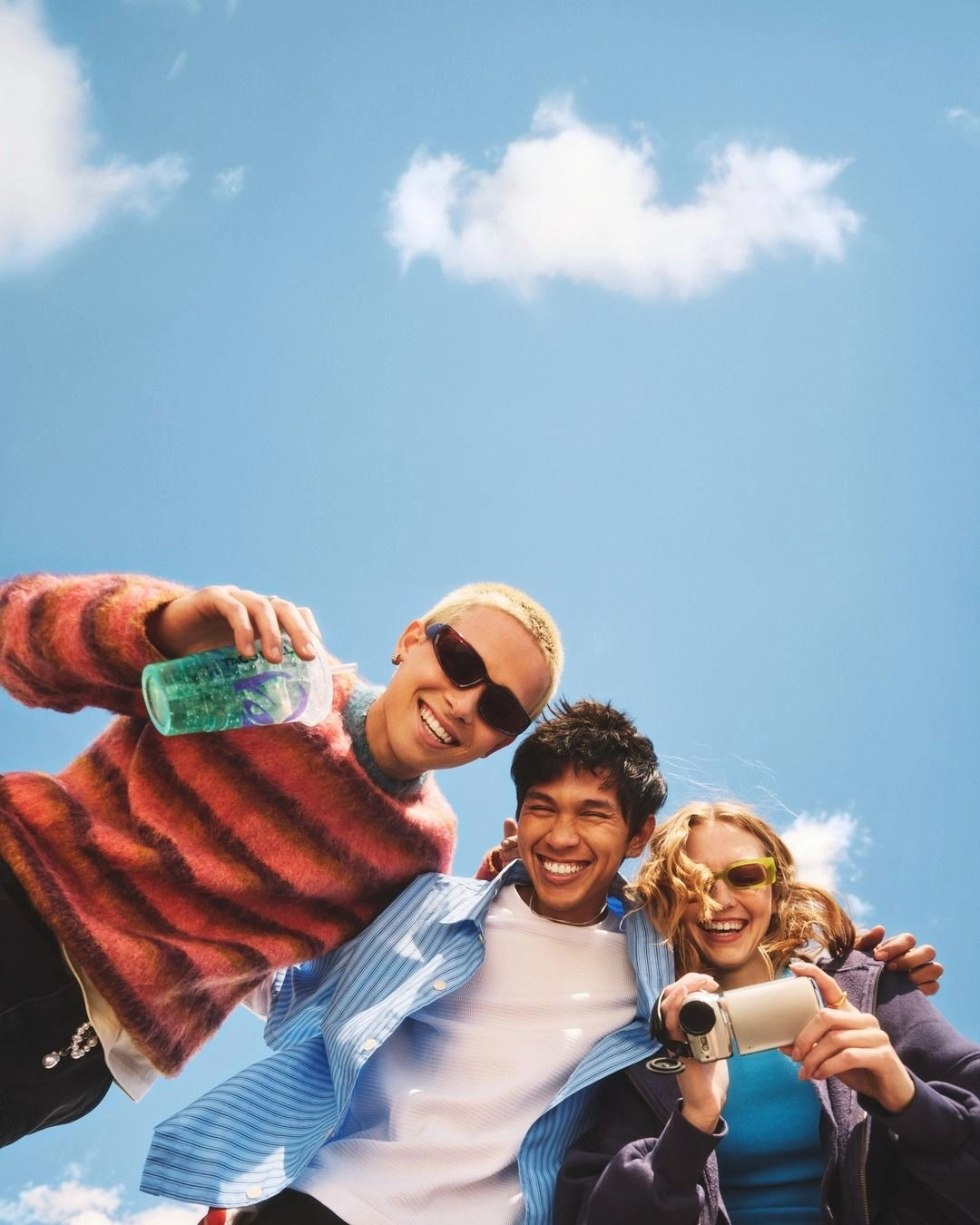 Three friends smiling together beneath a blue sky